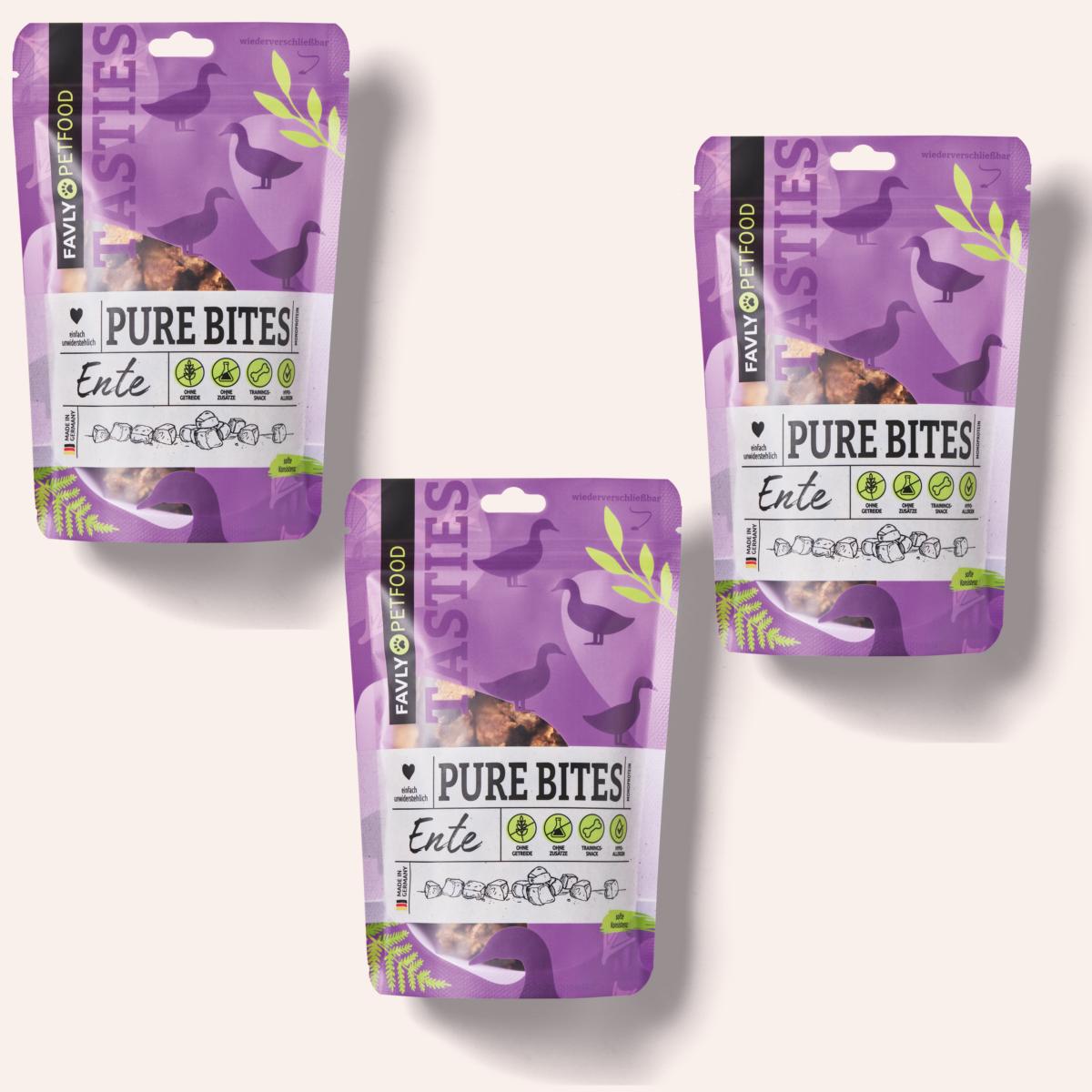 Drei Beutel mit Hundeleckerlis mit der Aufschrift „PURE Bites Ente“ von FAVLY Petfood, mit Abbildungen von Enten und lila Verpackung, werden ausgestellt. Diese Hundesnacks sind mit natürlichen Zutaten und hochwertigem Entenfleisch für die Freude Ihres pelzigen Freundes ausgestattet.