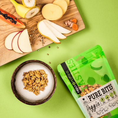 Schale mit Veggie-Snacks, geschnittenem Obst und FAVLY Petfood PURE Bites Veggie auf grünem Hintergrund.