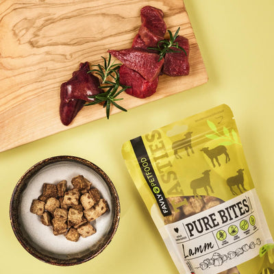 FAVLY Petfood PURE Bites Lamm auf einem Brett, Snacks in einer Schale und der Beutel auf gelbem Hintergrund.