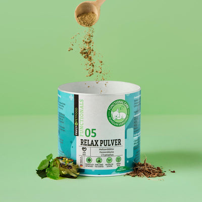 Ein Holzlöffel streut FAVLY Petfood Relax Pulver - Unruhe & Stress in eine Wanne auf grünem Hintergrund.