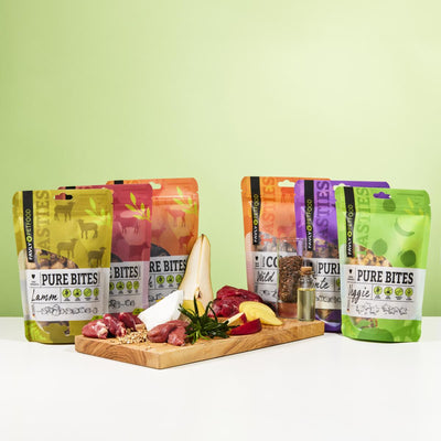 Fünf FAVLY Probierpaket "Snack it" von FAVLY Petfood hinter einer Tafel mit Fleisch, Käse und Birne.