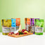 Vier FAVLY Probierpaket "Snack it" Tüten von FAVLY Petfood auf Holzbrett vor grünem Hintergrund.